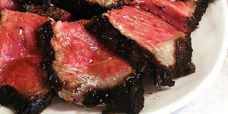 Su un piatto bianco sono disposte diverse fette di bistecca di media cottura, con una crosta carbonizzata e stagionata e un centro succoso e rosa, che evidenziano sia il fascino culinario sia l'importanza di evitare l'intossicazione alimentare rischi e soluzioni assicurative.