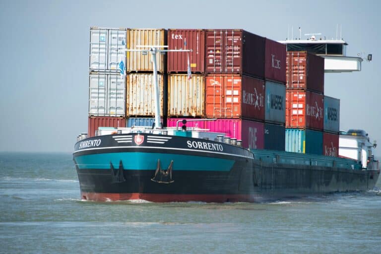 A cargo ship named Sorrento sails on the water, carrying multiple stacked shipping containers in red, orange, yellow, and blue—highlighting the global trade where commercial credit risk and unpayment invoices are everyday concerns.