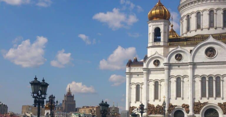 Una cattedrale bianca con cupole dorate e dettagli ornamentali sulla destra, sullo sfondo di un cielo blu; lampioni neri ed edifici cittadini suggeriscono una Russia vibrante, dove le attività di importazione, esportazione e distribuzione prosperano in un elegante contesto urbano.